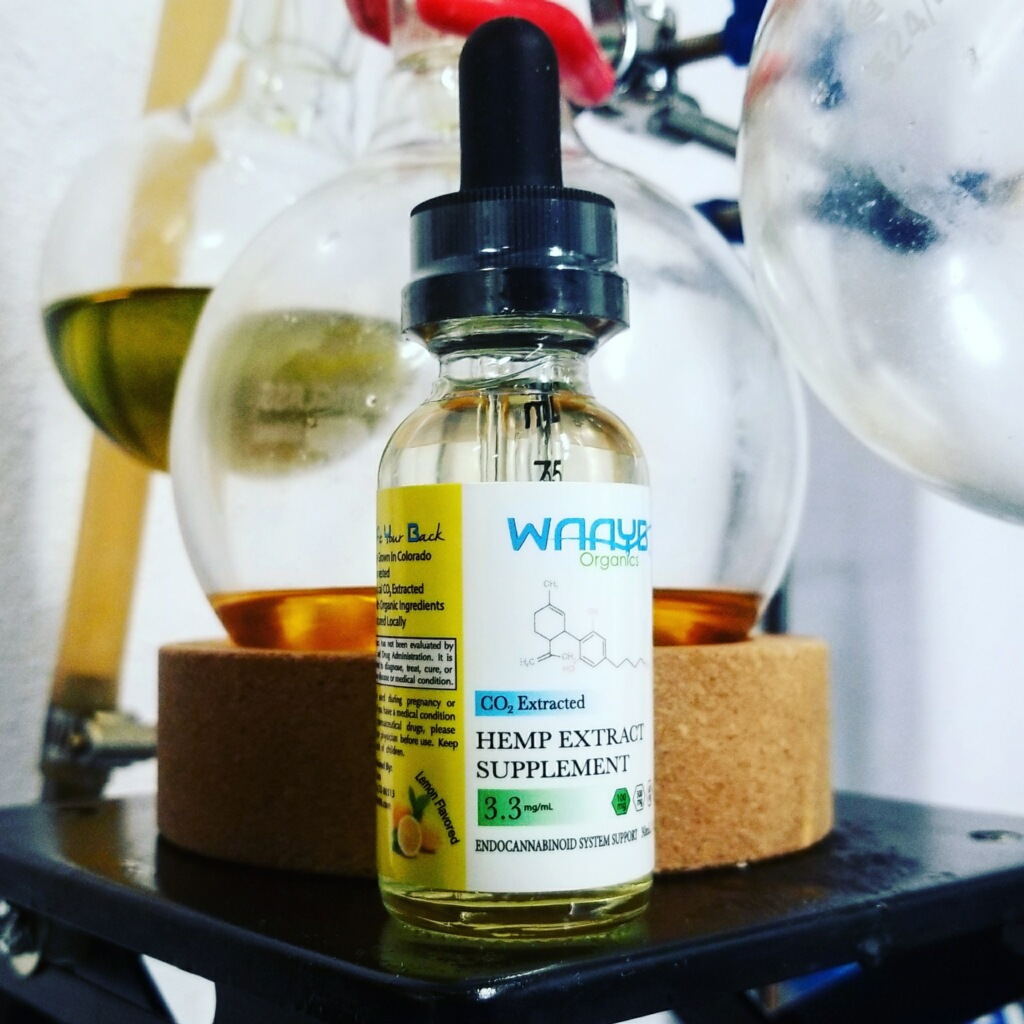 A bottle of Waayb Organics hemp extract on a lab bench, extraction glassware behind it.
